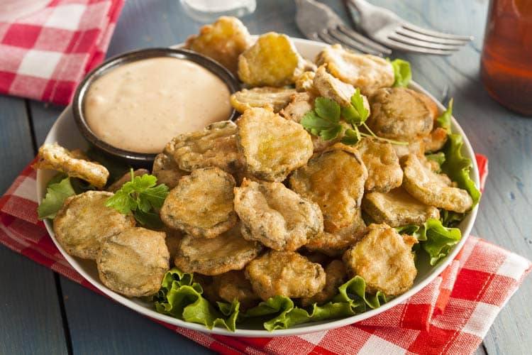 crispy fried pickles served with dipping sauce on a white plate