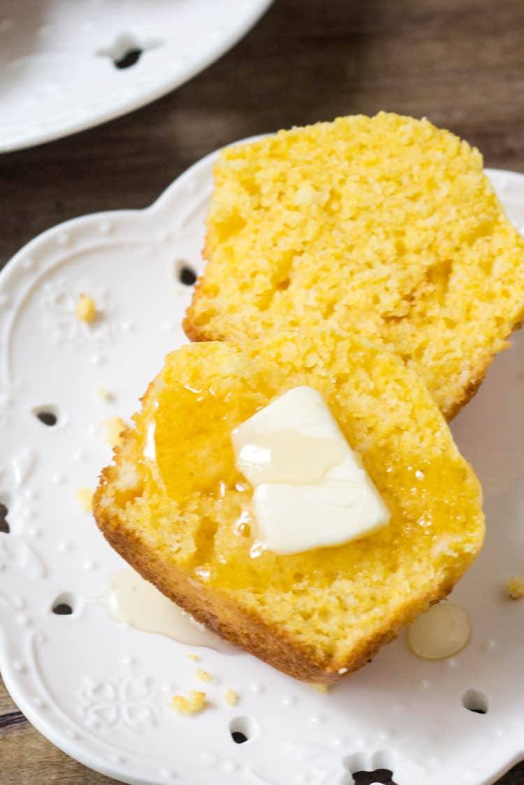 a cornbread muffins sliced in half wth a slab of butter
