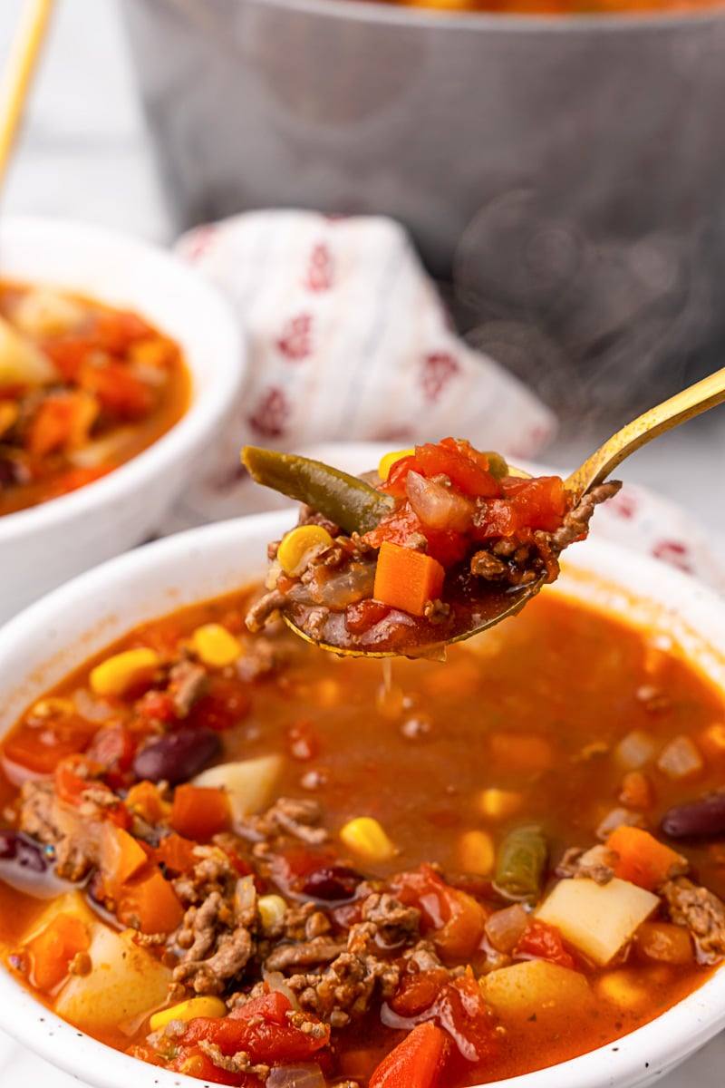 Gold spoon lifting a bite of Crazy-Easy Cowboy Soup with beef, corn and tomatoes over a steaming bowl