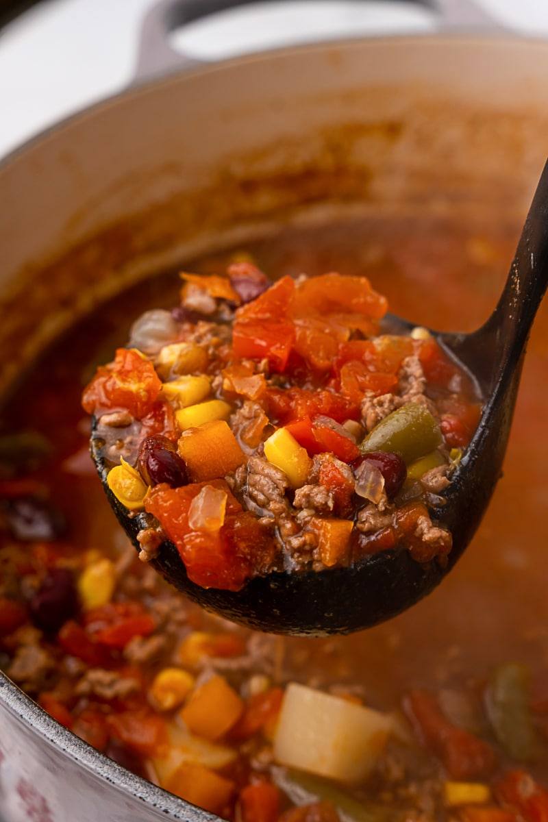 Ladle scooping Crazy-Easy Cowboy Soup with beef, beans and vegetables from a Dutch oven