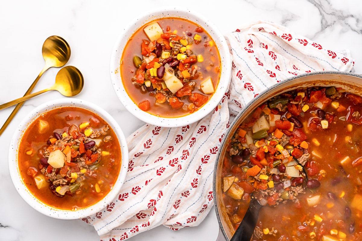 Overhead view of two bowls of Crazy-Easy Cowboy Soup with beef, beans and potatoes on a marble counter
