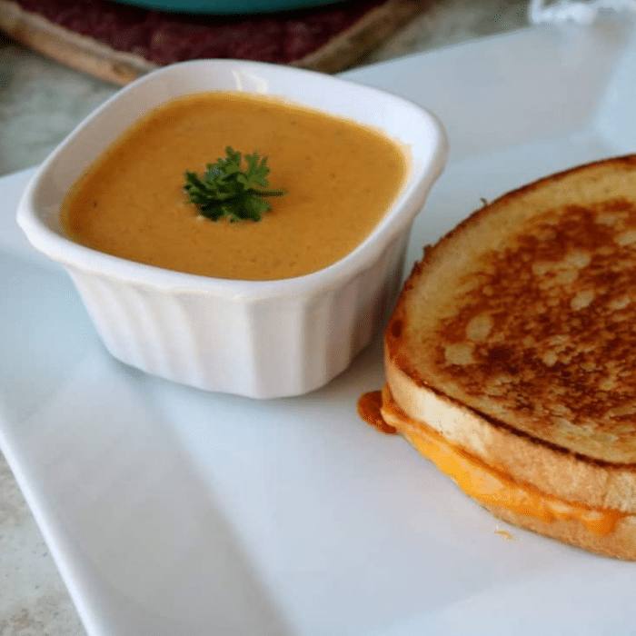 Creamy carrot soup in a white ramekin next to a grilled cheese sandwich