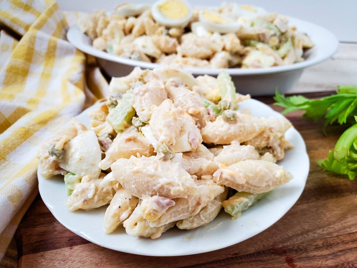 side view of plate of creamy tuna egg pasta salad next to serving dish