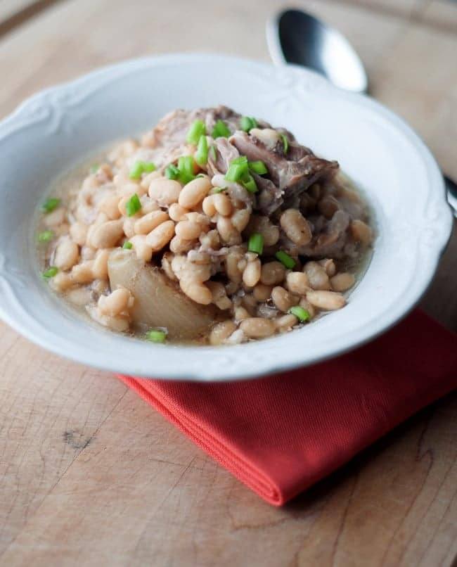 Bowl of slow cooker white beans and ham garnished with chives on a red napkin