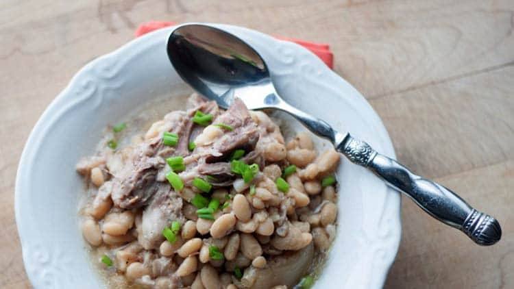 Crock pot ham and white beans served in a white bowl with a vintage spoon