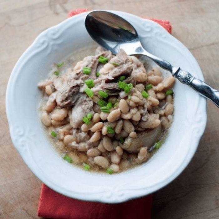 Crock pot ham and white beans in a white bowl with a spoon