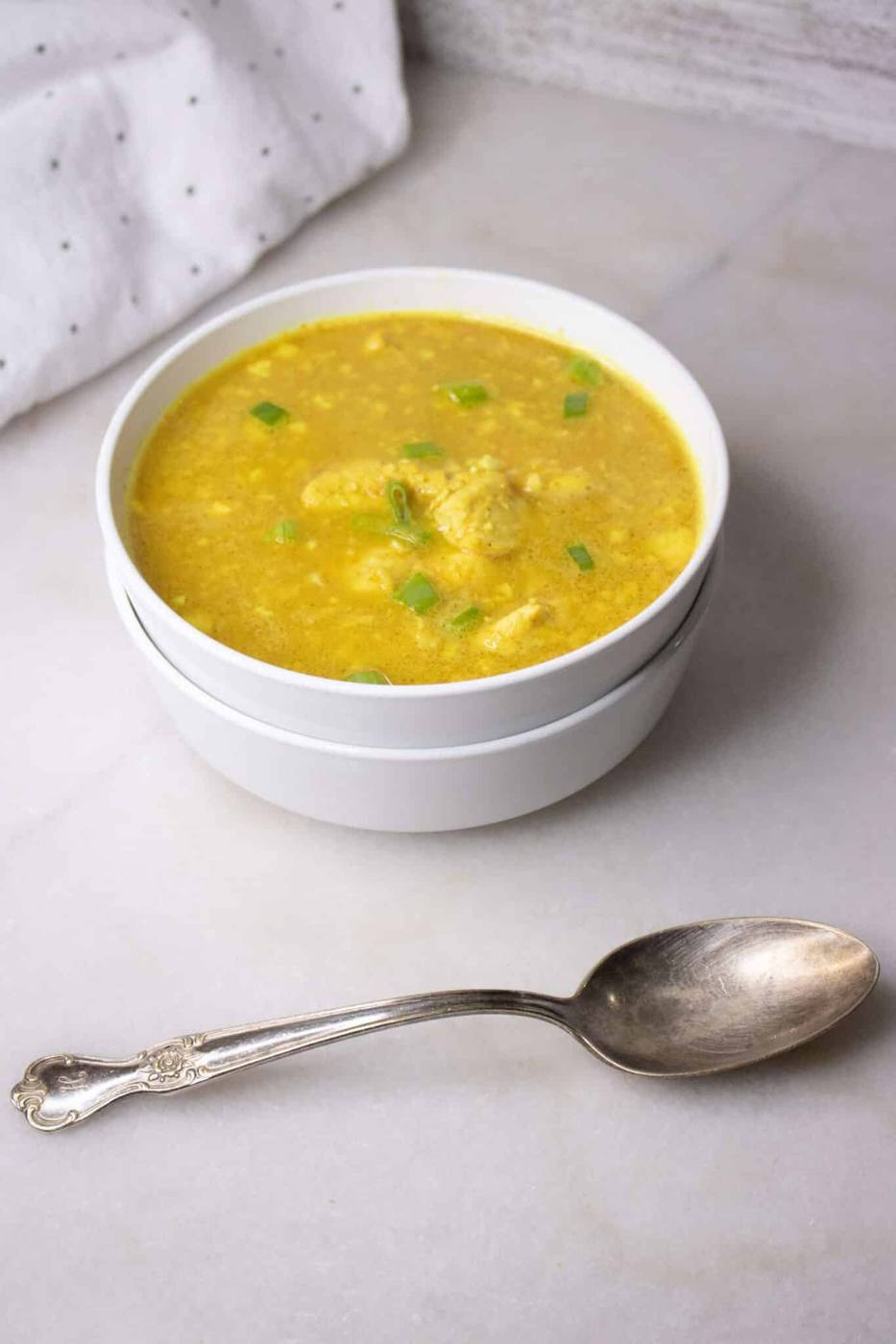 Curried chicken and cauliflower rice soup in a white bowl with a vintage silver spoon