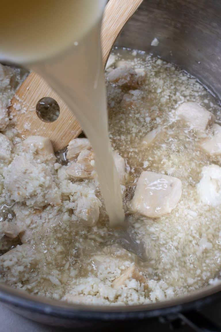 Liquid being poured into the pot of chicken and cauliflower rice for curried chicken soup