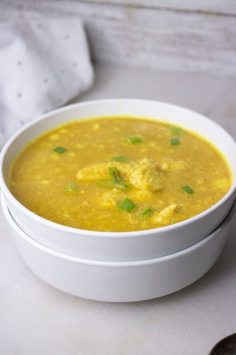 Curried chicken and cauliflower rice soup topped with green onions in stacked white bowls