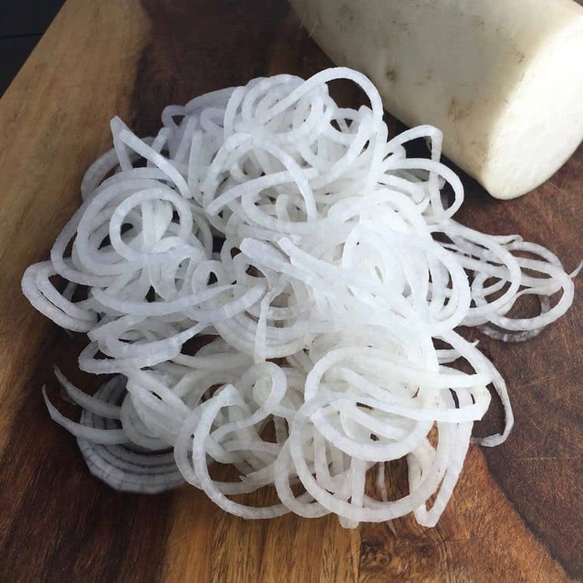Spiralized daikon noodles piled on a wooden cutting board next to a whole daikon radish