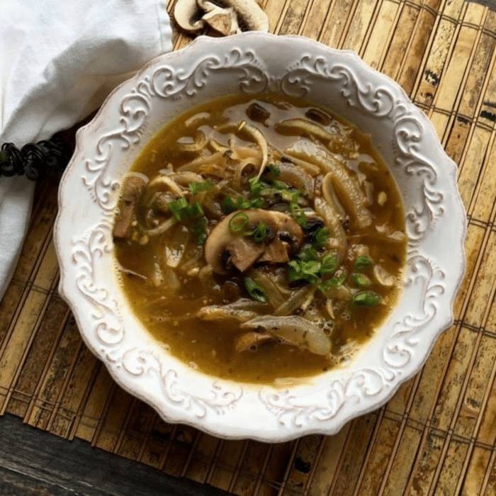 Daikon noodle soup with caramelized onions, mushrooms and green onions in a white scalloped bowl