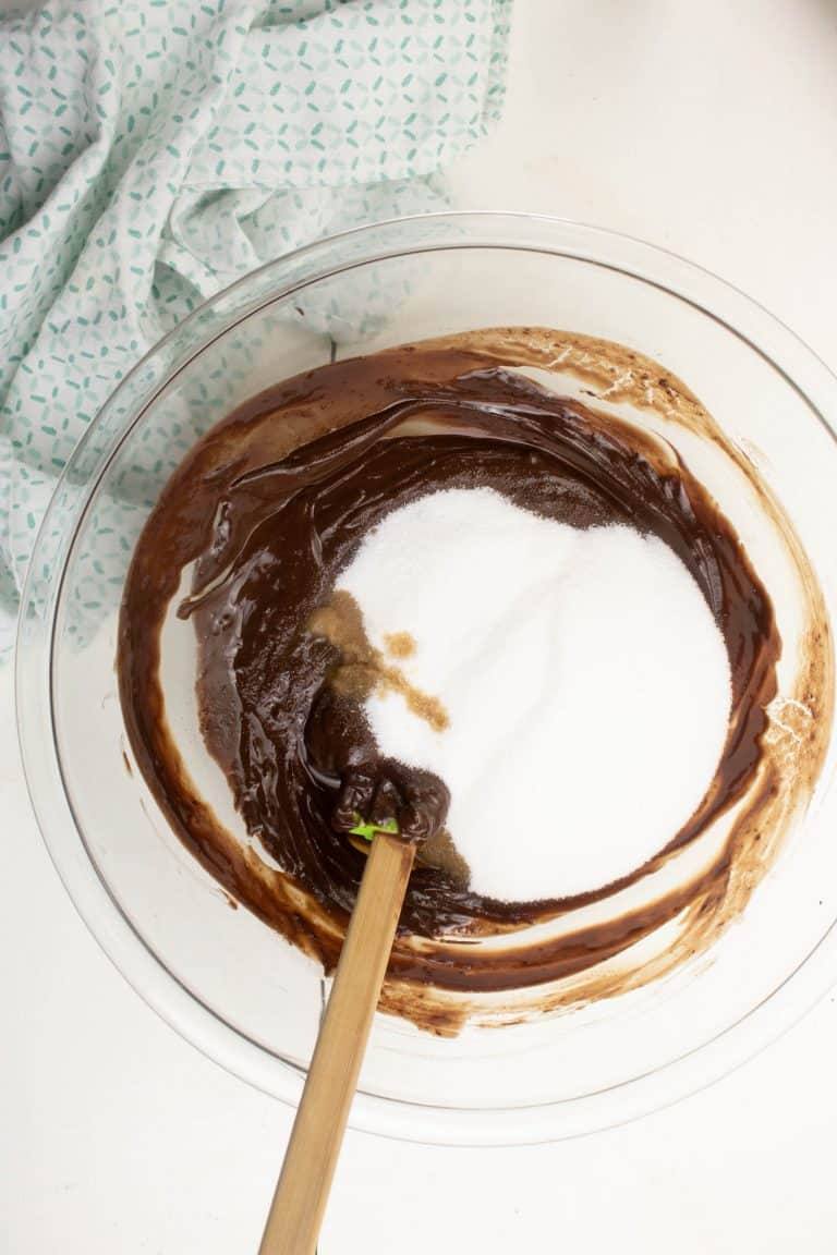Clear glass bowl with chocolate batter and sugar for Dark chocolate brownies with spatula and blue white towel.