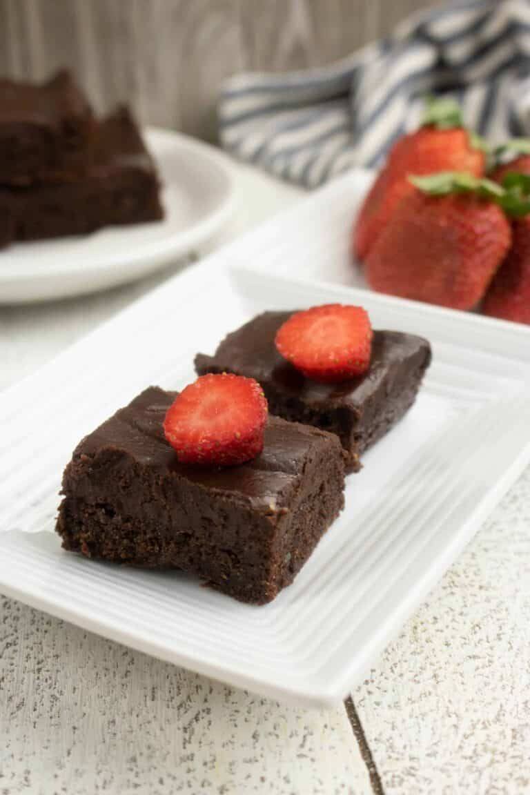 2 dark chocolate brownies on white plate with strawberry slices on top