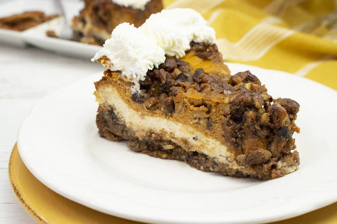 Slice of double layer pumpkin cheesecake with pecan crust and whipped cream on a white plate
