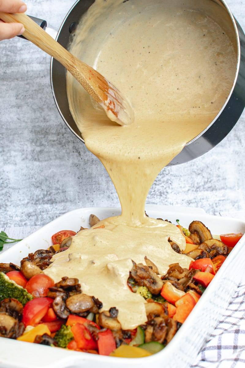 pouring cheese sauce over vegetables