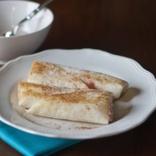Two golden tortilla cream cheese roll-ups dusted with cinnamon sugar on a white plate