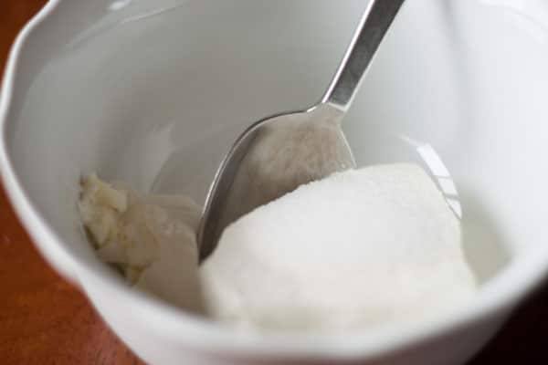 Softened cream cheese and sugar in a white mixing bowl with a spoon
