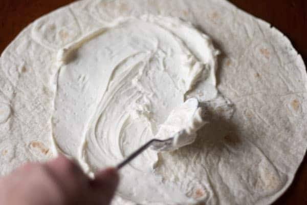 Spreading sweetened cream cheese over a flour tortilla with a spoon