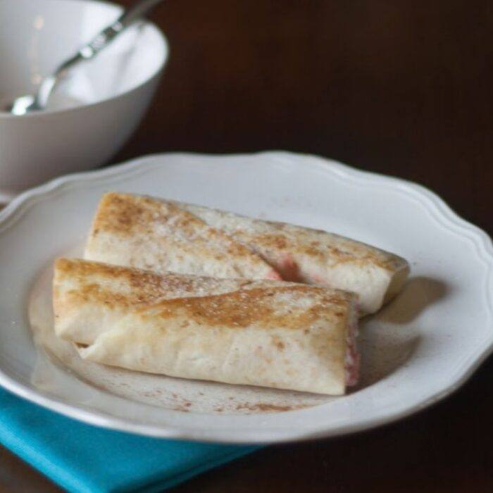 Tortilla cream cheese cinnamon roll-ups dusted with cinnamon sugar on a white plate