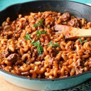 Skillet of chili mac with a wooden spoon on a teal table