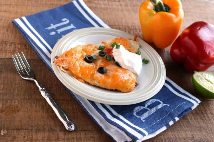 slice of mexican pizza topped with olives and sour cream on a white plate with a blue folded napkin