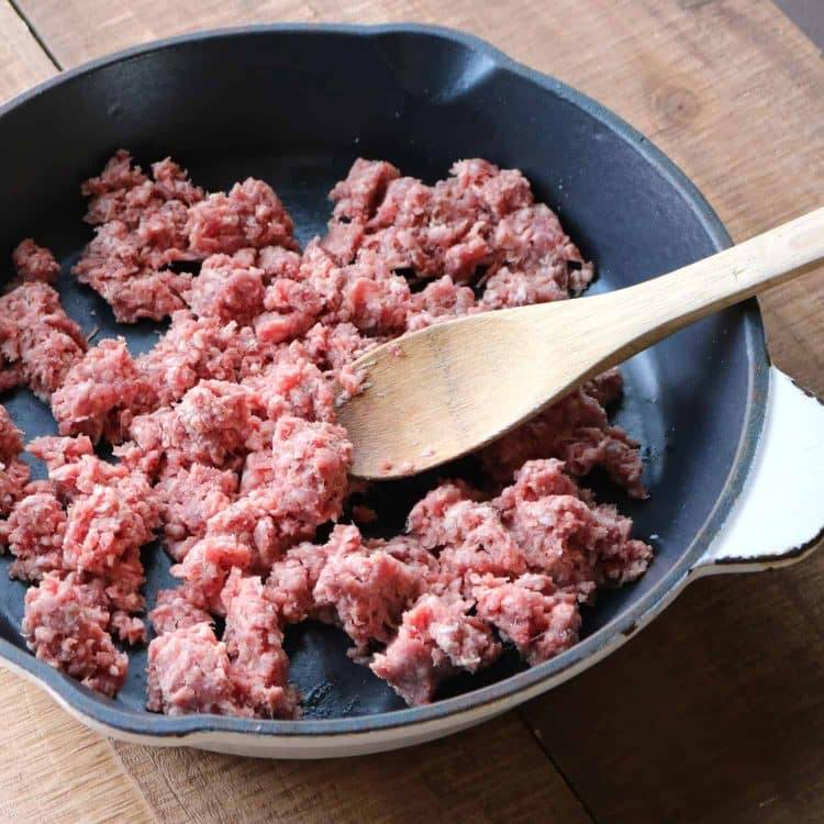 cooking ground beef in an iron skillet with a wooden spoon to make mexican pizza
