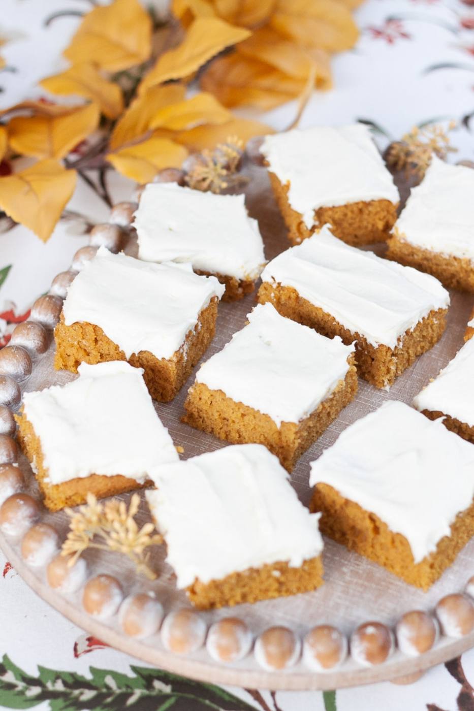 Frosted easy pumpkin bars cut into squares on a beaded wooden serving tray with fall leaves