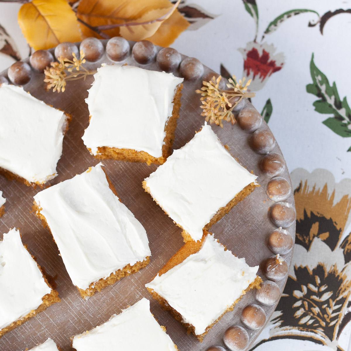 Overhead view of cream cheese frosted pumpkin bars on a beaded wooden tray
