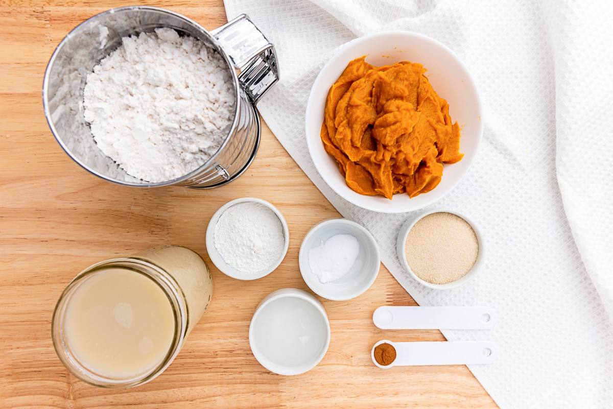 Pumpkin waffle ingredients including flour, pumpkin puree, milk, sugar, and spices on a wooden board
