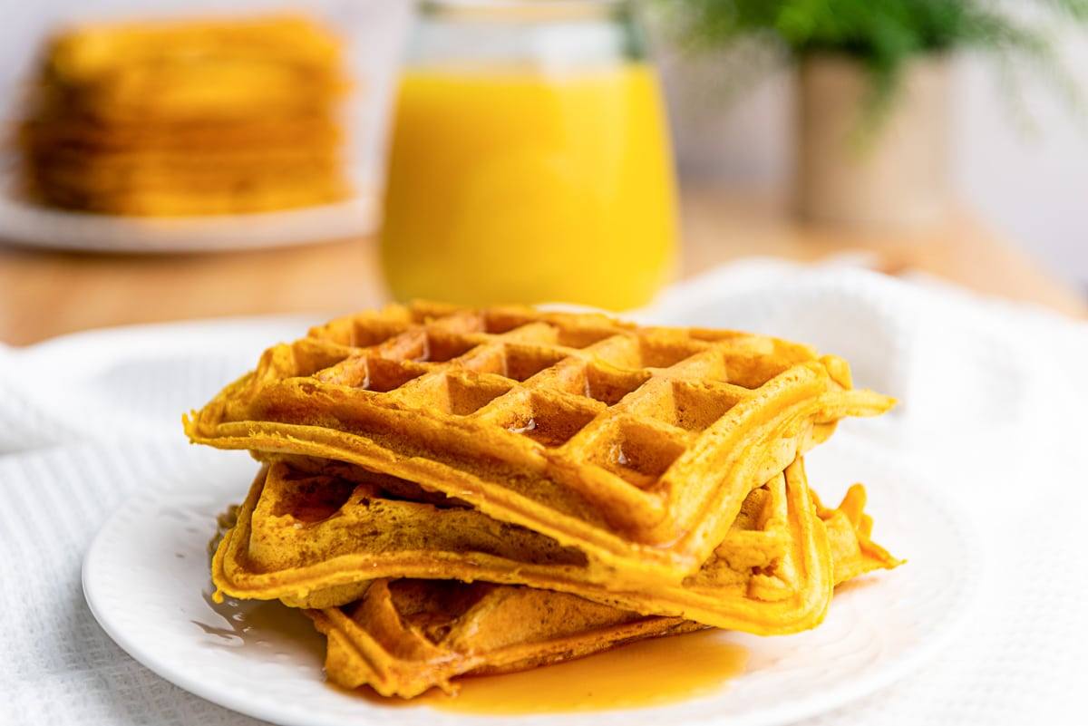 Side view of a stack of pumpkin waffles with maple syrup on a white plate