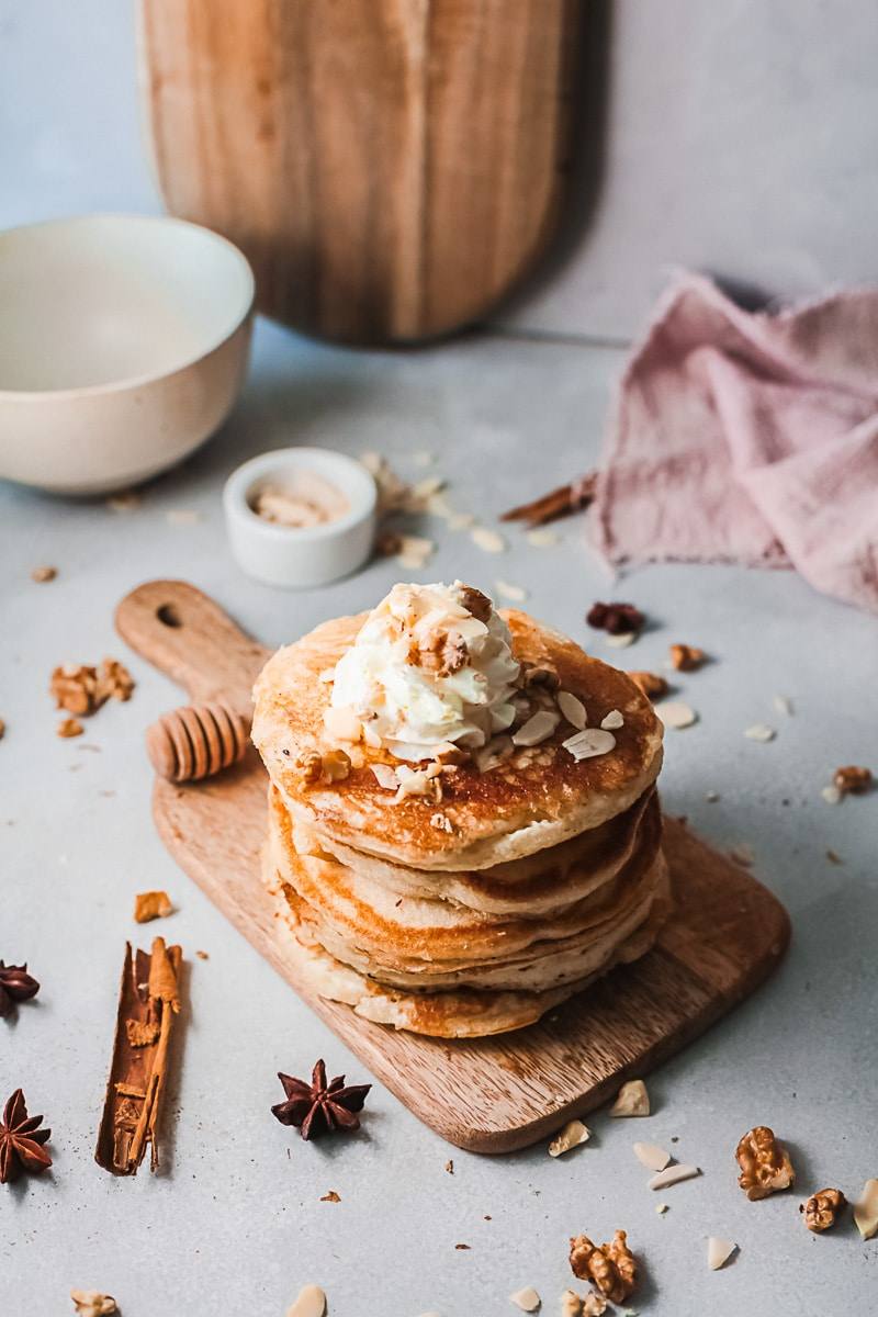 eggnog pancakes topped with nuts and whipped cream, being served on a wooden board