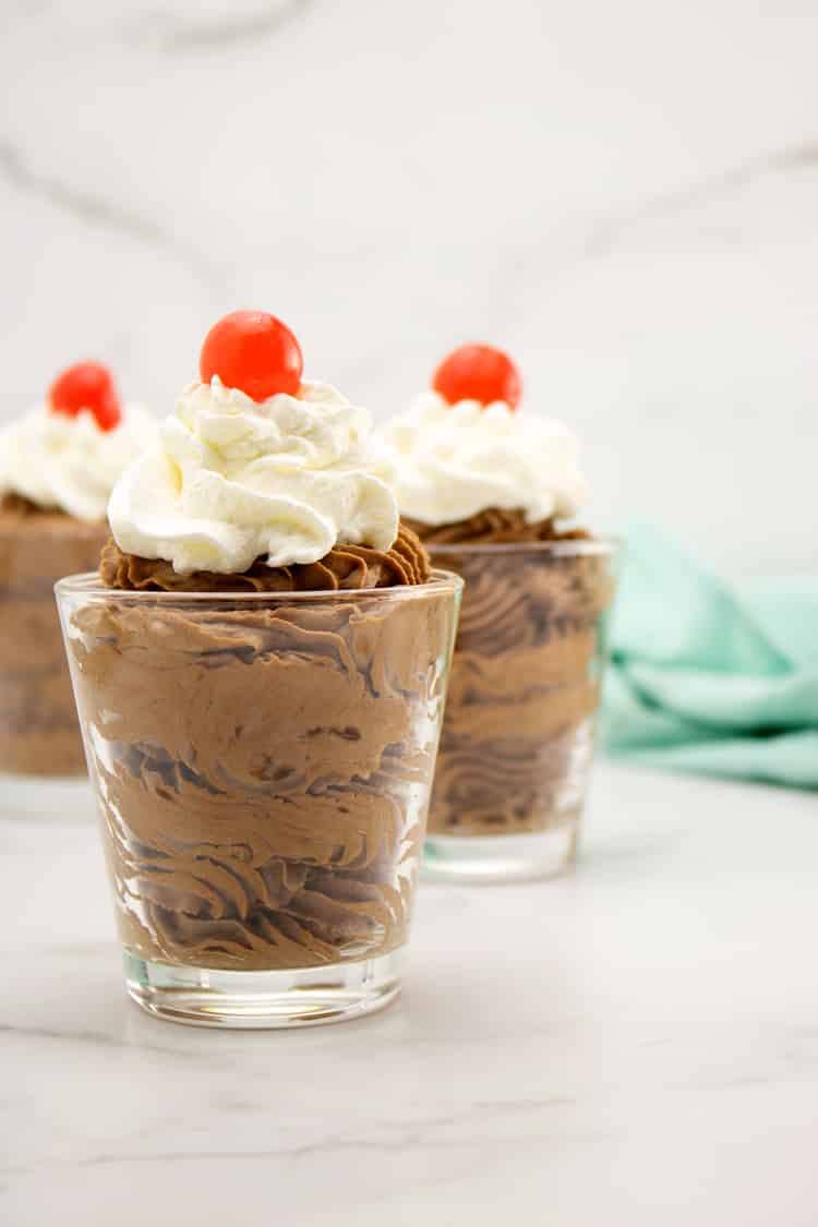 chocolate mousse in three glass dishes with whipped cream and cherry on top