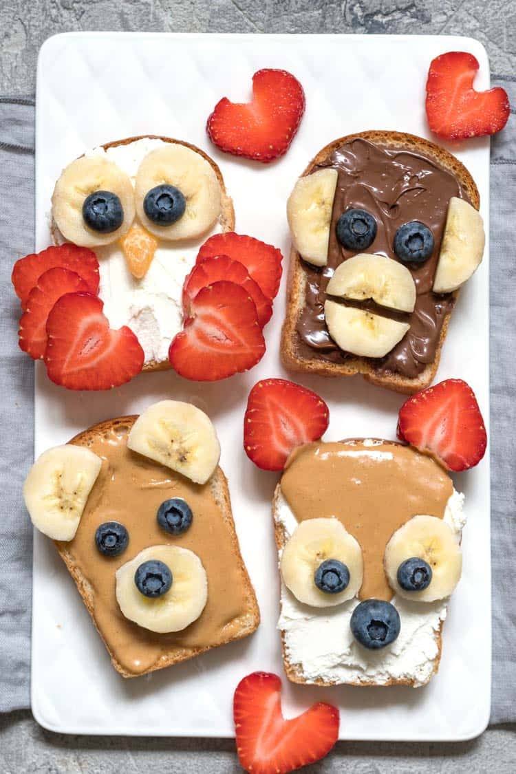plate full of animal face toasts, toasts decorated with fruit and breakfats preads to look like animal faces