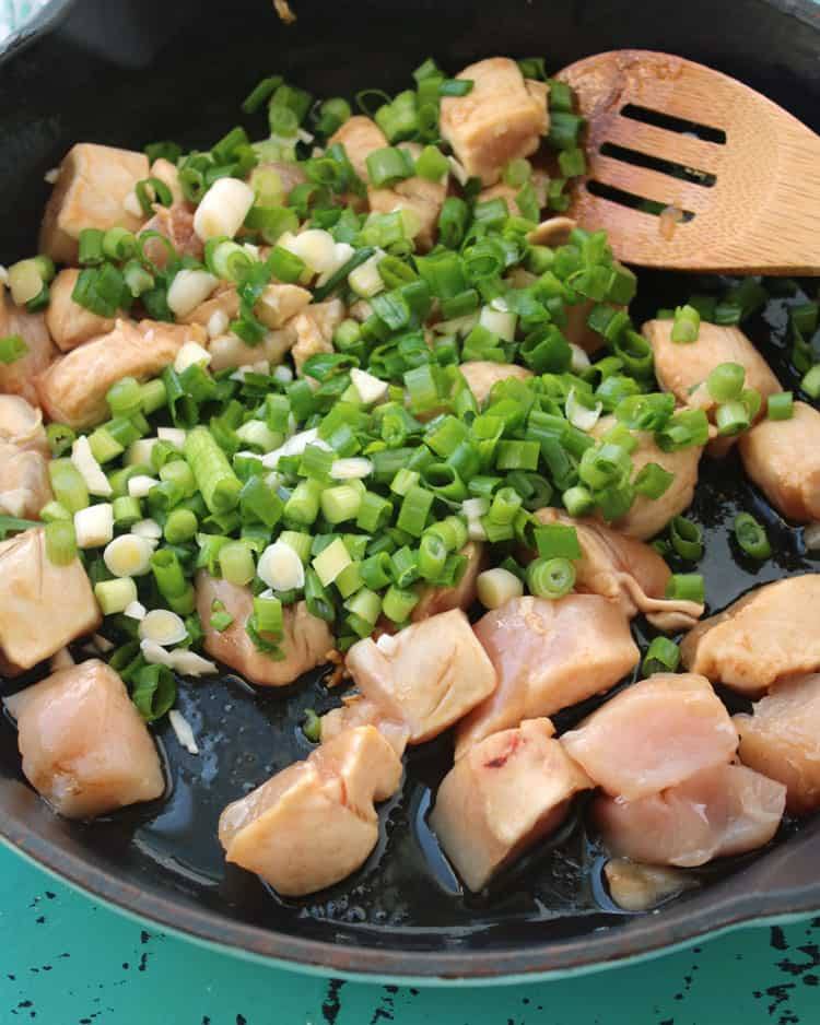 black pan containing chicken and scallions for chicken fried rice with wooden spoon