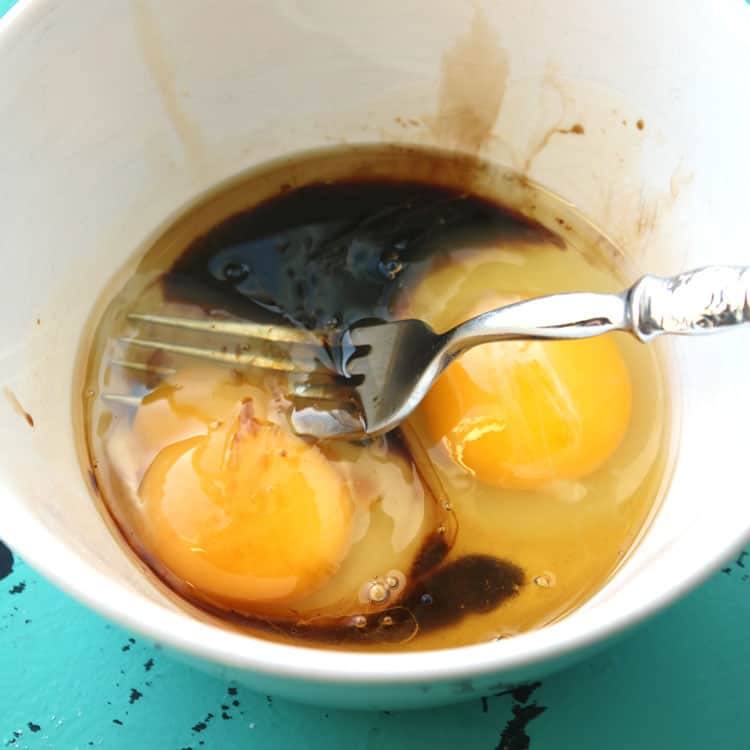 white bowl containing eggs, gluten-free soy sauce, and a fork to be used in chicken fried rice