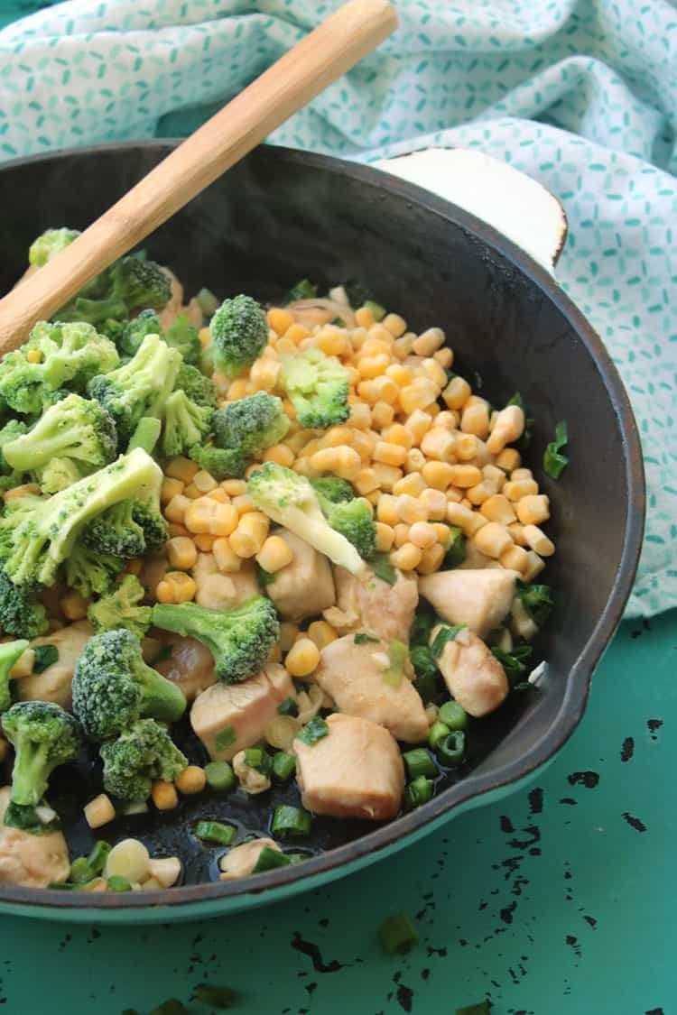 black cast iron pan containing cooked chicken and vegetables for chicken fried rice next to a blue and white towel