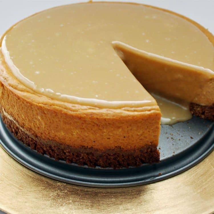 Whole maple pumpkin cheesecake on a gold cake board with one slice cut out