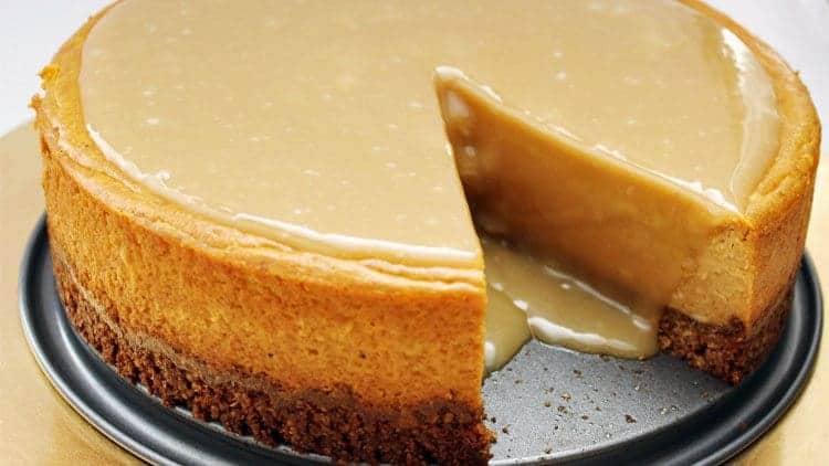 Pumpkin maple cheesecake on a springform pan base with a slice removed and maple glaze pooling