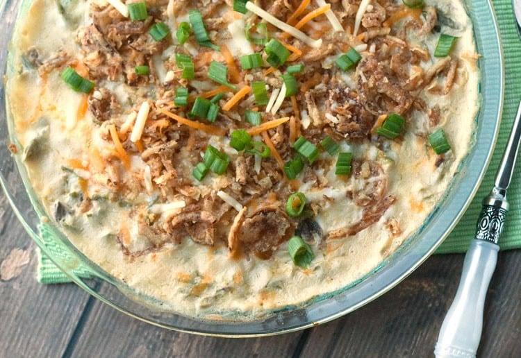 Baked green bean casserole topped with shredded cheddar, fried onions and sliced green onions