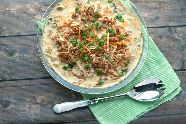 Creamy green bean casserole in a glass dish on a green napkin with a serving spoon