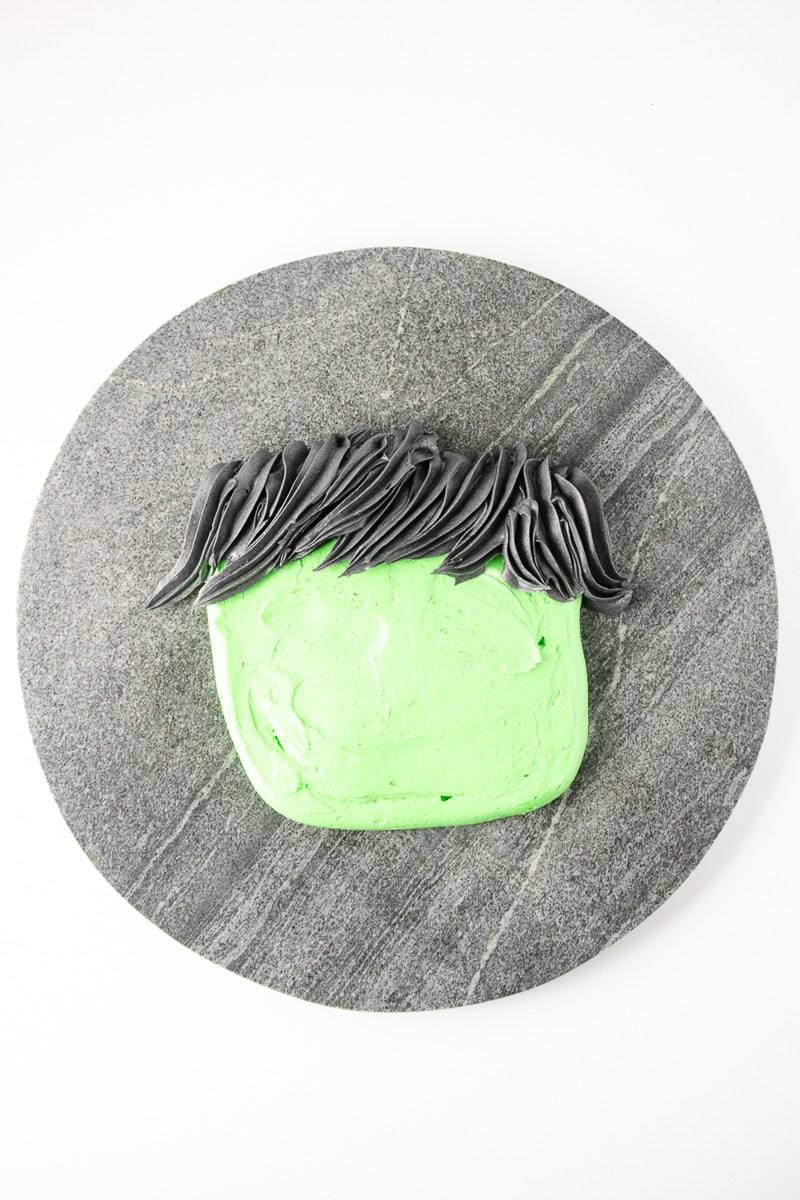Black buttercream hair piped with a star tip onto a green Frankenstein frosting face