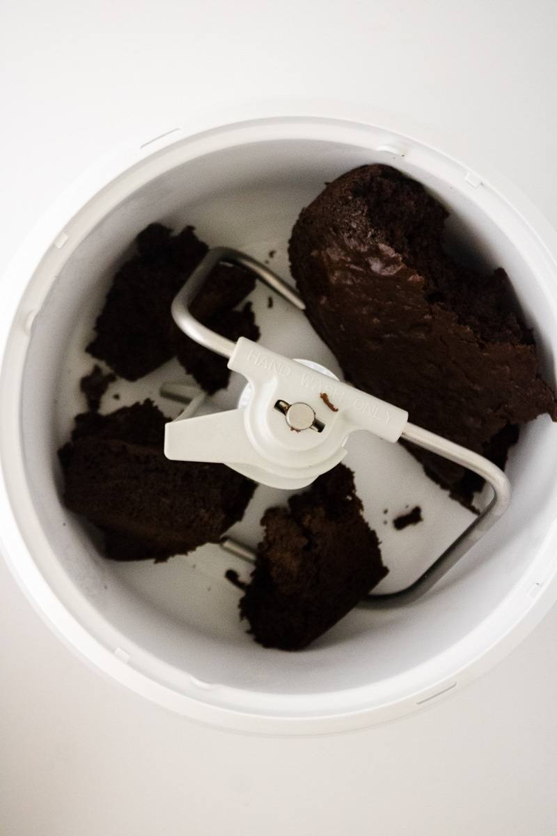 Chunks of baked chocolate cake in a stand mixer bowl with the paddle attachment