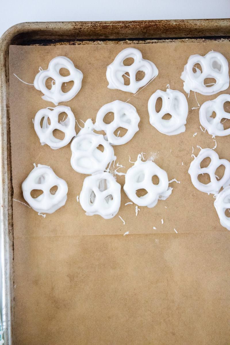 Mini pretzels coated in white candy melts setting on a parchment-lined baking sheet