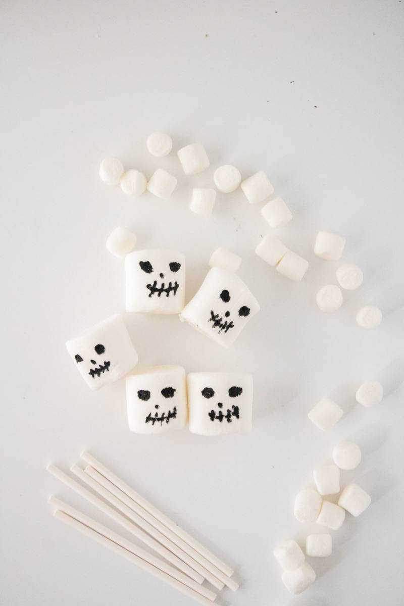 Large marshmallows with skeleton faces drawn in black edible marker, with mini marshmallows and lollipop sticks