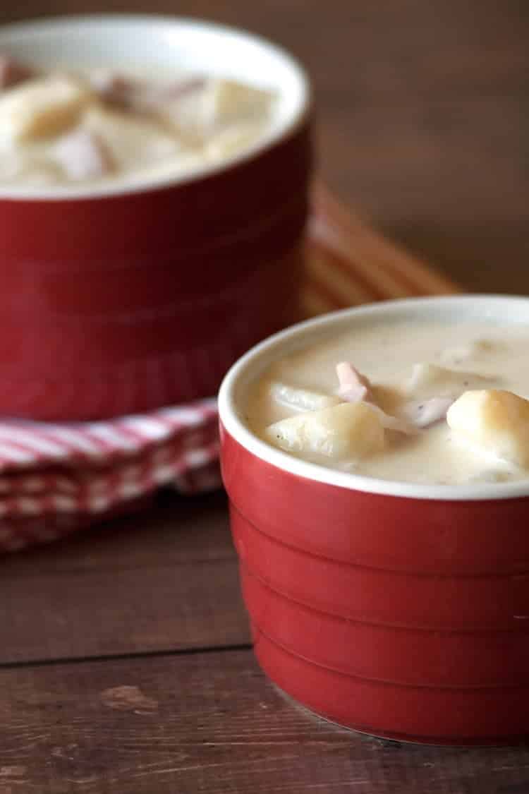Red ramekin filled with creamy ham and potato soup next to a striped napkin