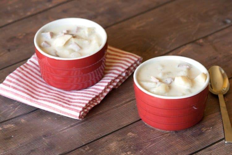 Two red bowls of creamy ham and potato soup on a striped napkin with a gold spoon
