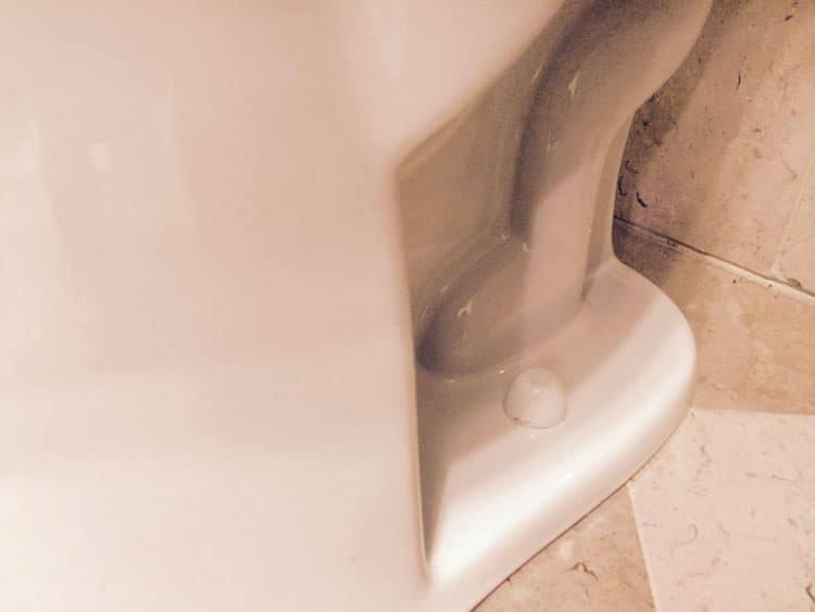 Close-up of the base of a white toilet where it meets the tile floor, including the bolt cap
