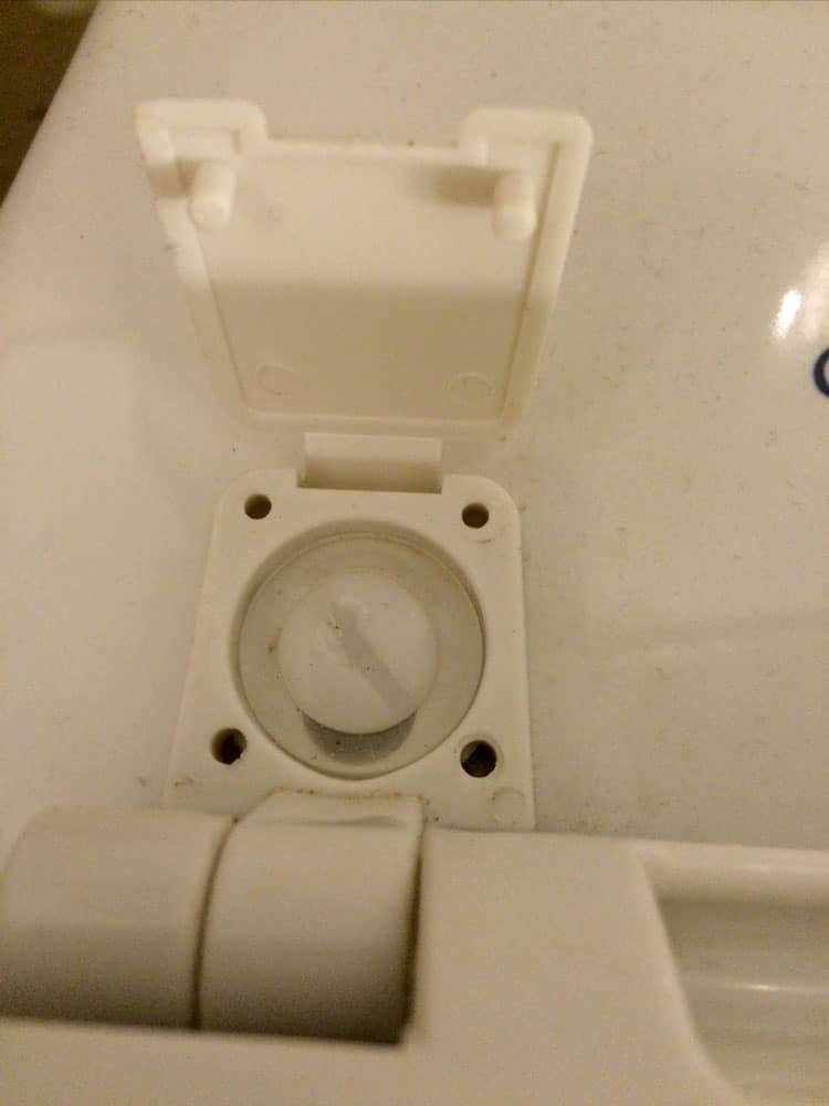 Toilet seat hinge with its plastic cover flipped open to show the bolt underneath