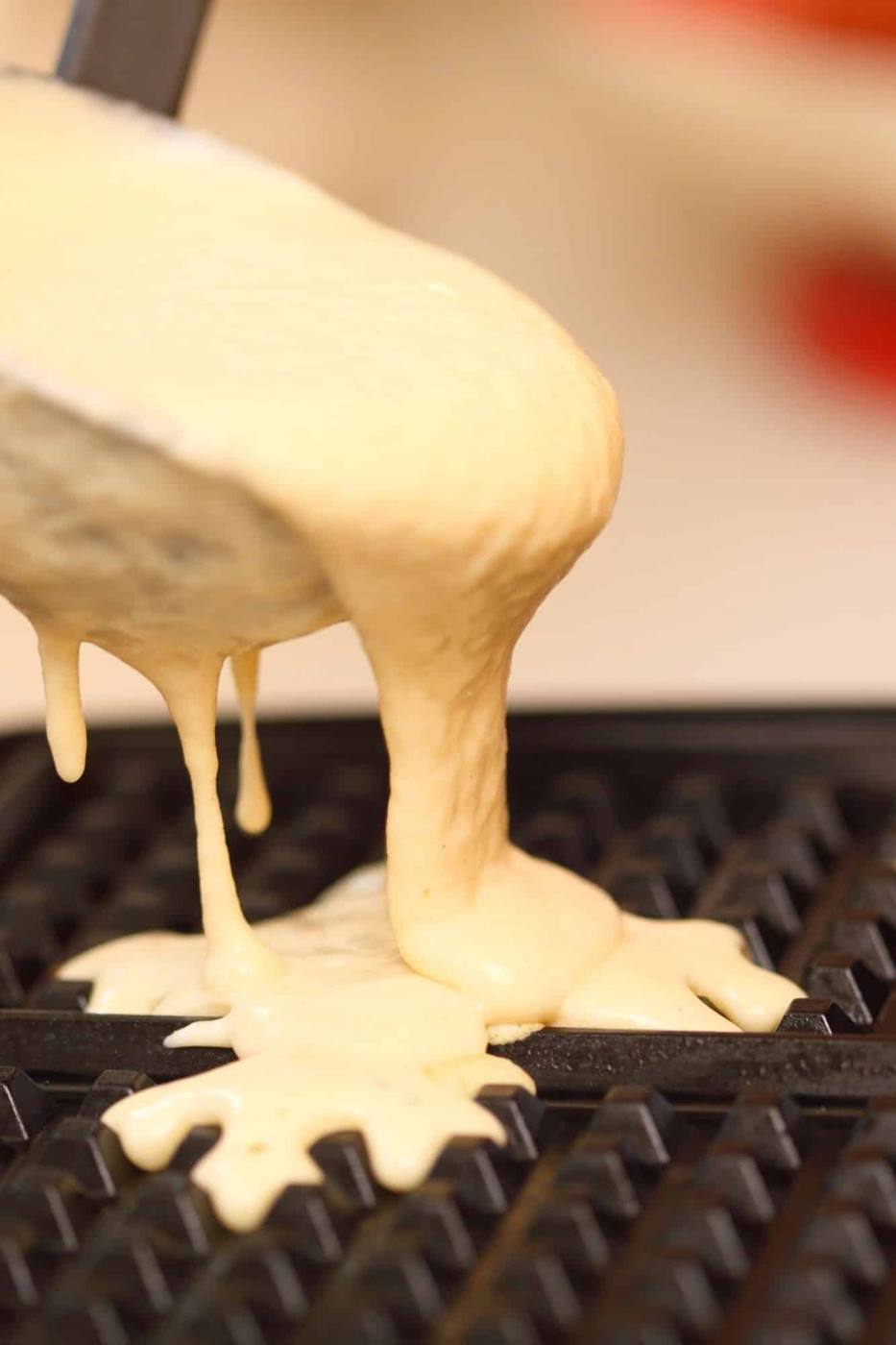 Waffle batter overflowing from a ladle onto a hot waffle iron griddle