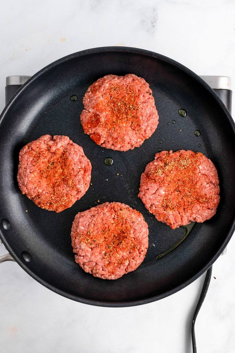 raw burger patties getting cooked in a skillet on the stove